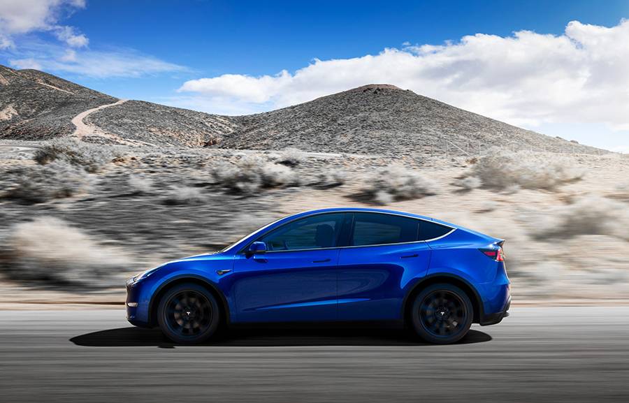 Kék színű Tesla Y oldalról fotózva menet közben